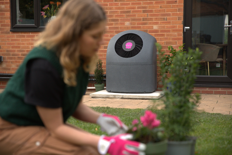 Woman gardening with pink gloves on and Octopus Cosy heat pump in background against brick wall of home