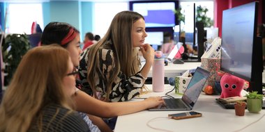Three people huddle around laptop, looking at it intently