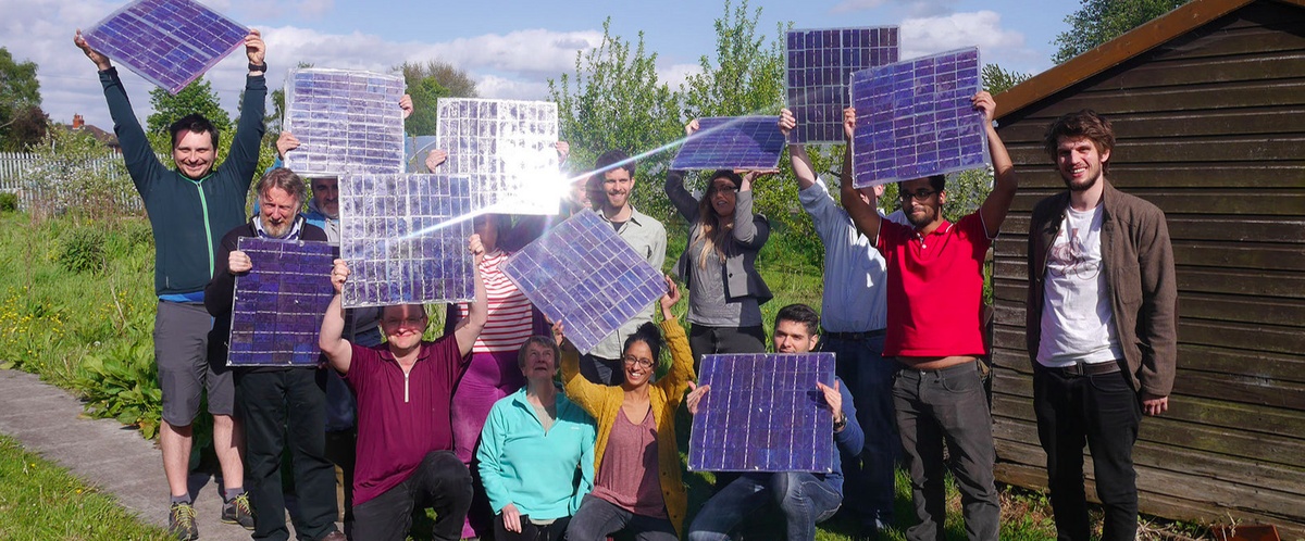 A picture of 9 community energy team members, each holding up a small solar panel.