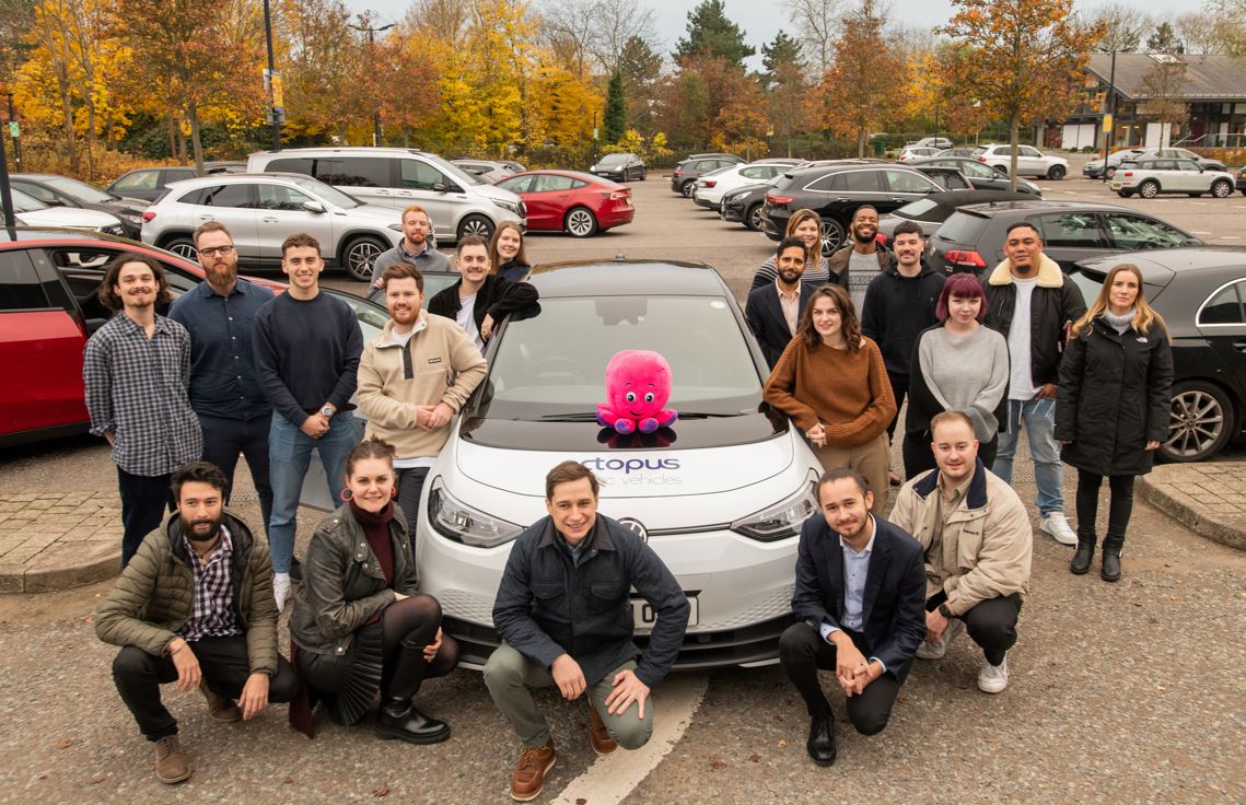 A picture of the EV team posing near a grey electric car