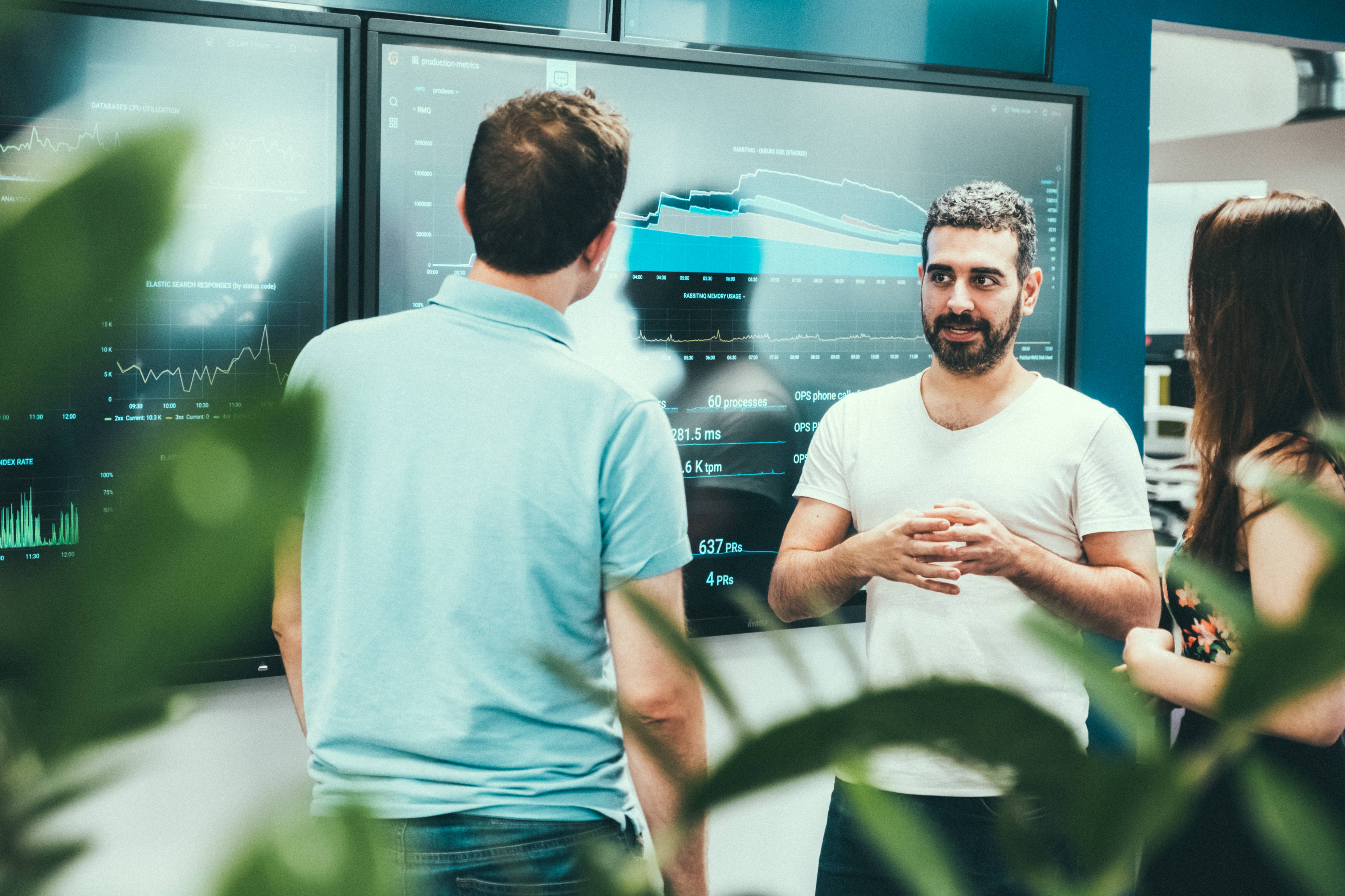 an image of two employees standing next to a wall mounted monitor