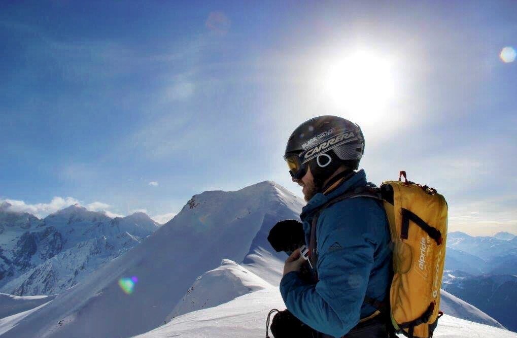 A photo of Alex Schoch with the sun behind him, at the top of a mountain