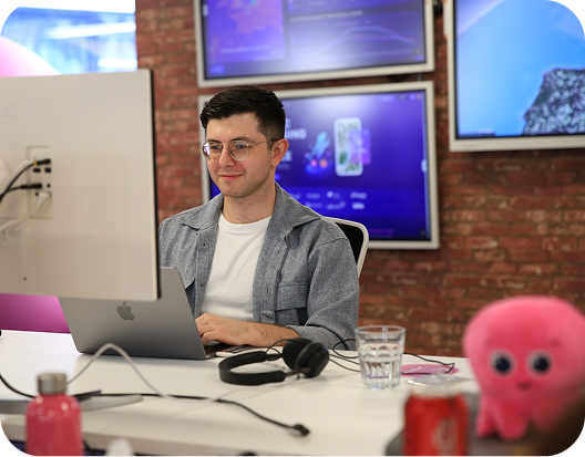 Energy Specialist in glasses with dark hair sits in front of his computer desk. There is a pink Octopus plushie at the side of his desk.
