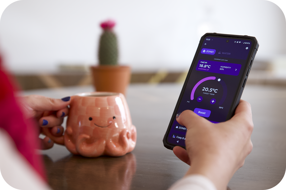 Close up shot of hand holding photo with Octopus app open, setting a Cosy schedule for their heat pump. In the other hand, the person is holding an Octopus mug.